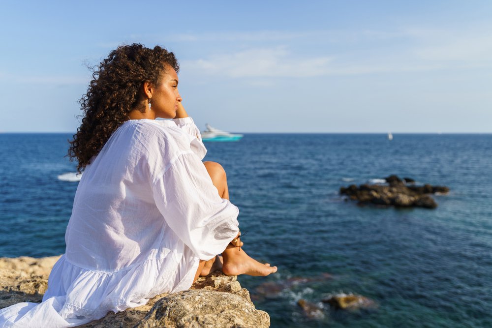 Curly haired woman sitting and looking at the landscape. Freedom concept